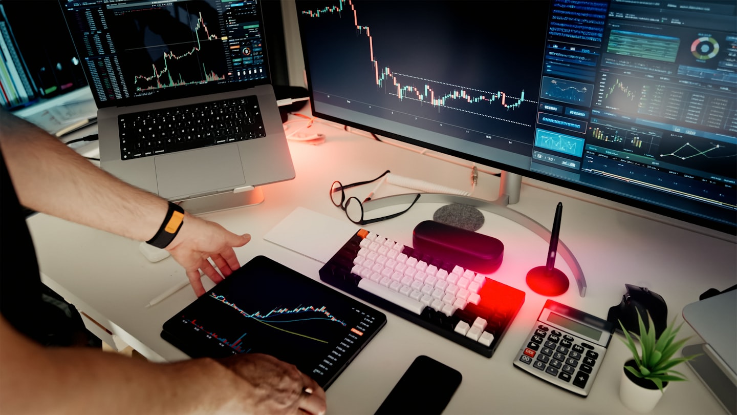 Modern ofiste finansal grafiklerin olduğu bir tableti kullanan eller.